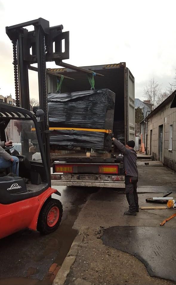 A wrapped printing machine being lifted into a shipping container by forklift