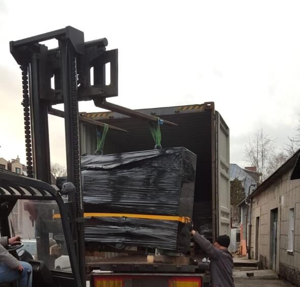 Shrink-wrapped printing machine being lifted into a shipping container by forklift